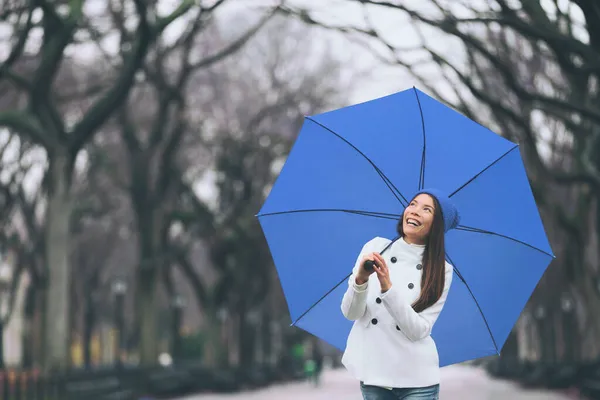 冬天的妇女在雪地的森林公园里散步，带着蓝色的雨伞，享受户外的雪景。在纽约中央公园快乐的亚洲女孩. — 图库照片