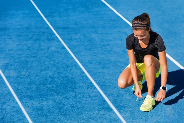 Sprinter koşucusu dışarıdaki atletizm pistinde koşmaya hazırlanıyor. Mavi pistlerde yarışmak için bağcıklarını bağlayan kadın sporcu — Stok fotoğraf