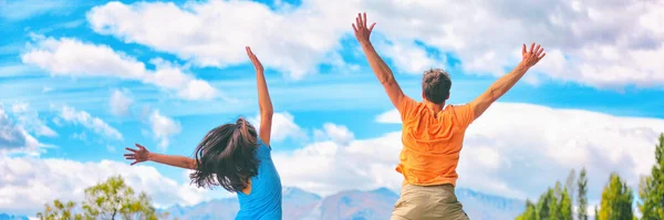 Des gens heureux sautant de plaisir en profitant de l'aventure de voyage. Jeune couple de derrière bonheur saut bannière panorama dans le ciel bleu. — Photo