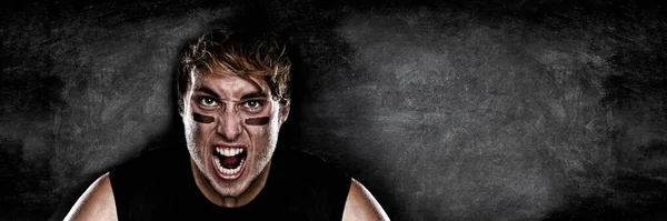 American football player screaming on black chalkboard texture background copy space for advertising. Panoramic banner blackboard with man athlete ready to play face paint black eye. — Stock Photo, Image