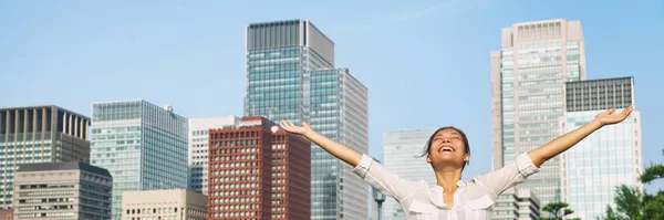 Счастливая азиатка с распростертыми объятиями, дышащая свежим воздухом на фоне городских зданий. Бизнесмен на работе улыбается баннерной панорамой. — стоковое фото