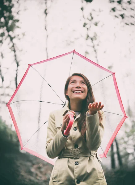 Jesienna kobieta spacerująca w deszczu z parasolem. Azjatycki model spoglądający w górę na deszczowy jesienny dzień z rozdaniem i płaszczem przeciwdeszczowym na zewnątrz w lesie natury. Wielorasowy Azji dziewczyna. — Zdjęcie stockowe
