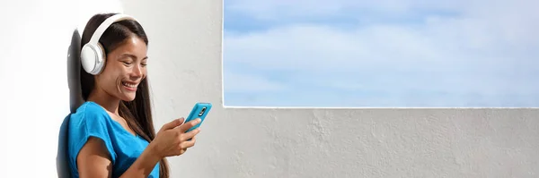 Chica viendo un video en su teléfono móvil escuchando música con auriculares inalámbricos en el balcón de su casa. Sonriendo mujer asiática disfrutando de usar su teléfono inteligente fuera en el estilo de vida de verano. — Foto de Stock