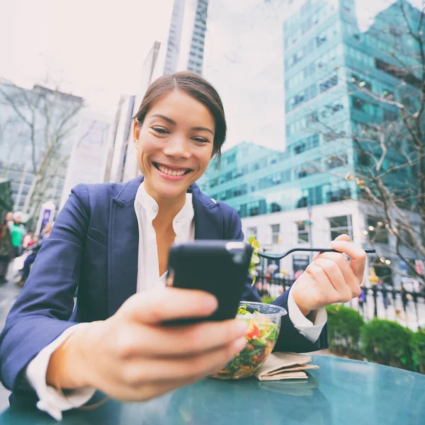 Akıllı telefondaki genç iş kadını öğle yemeği molasında salata yiyor sağlıklı bir hayat sürüyor akıllı telefon üzerinde çalışıyor. Mutlu melez Asyalı iş kadını, New York City, ABD — Stok fotoğraf