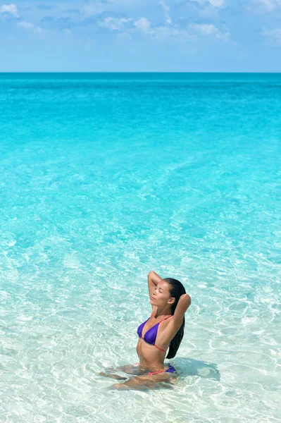 Bikini body beach swimwear model swimming in idyllic turquoise ocean water relaxing under the sun. Mulher asiática tocando seu cabelo saudável em maiô corpo bronzeador. — Fotografia de Stock