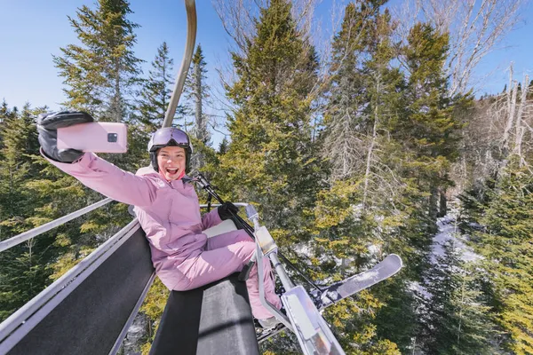 Vacaciones de esquí - Mujer esquiadora en telesilla haciendo foto autofoto o video usando el teléfono. Esquí concepto de vacaciones de invierno. Esquí en las pistas de nieve en las montañas, La gente se divierte en el día nevado. Actividad deportiva de invierno. — Foto de Stock