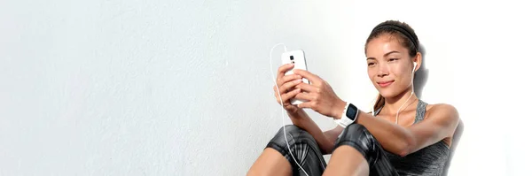 Mulher asiática assistindo vídeos de fitness online usando telefone celular ouvindo música com fones de ouvido e smartwatch. Panorama da bandeira tecnológica. Estilo de vida ativo. Dispositivo de tecnologia vestível de esportes. — Fotografia de Stock