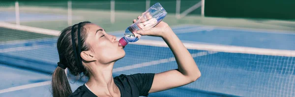 Sediento Deportiva chica asiática beber agua mientras juega al tenis en la cancha al aire libre. Deportes estilo de vida activo mujer hidratante con botella de deportes acuáticos. Panorama banner. — Foto de Stock