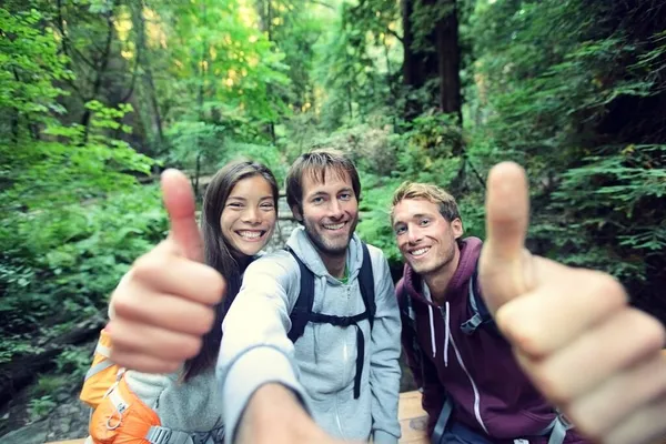 Caminhadas grupo de amigos viajar estilo de vida jovens felizes fazendo polegares para cima na foto selfie. Três jovens homens e mulheres se divertindo mochila na natureza camping. — Fotografia de Stock