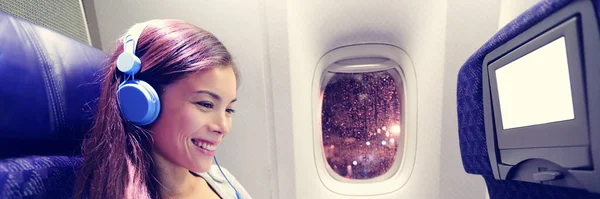 Pasajero en avión usando tableta. Mujer en cabina de avión usando un dispositivo inteligente escuchando música en auriculares. Pancarta panorámica viajes gente estilo de vida. —  Fotos de Stock