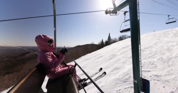 Vacaciones de esquí - Mujer esquiadora usando el teléfono en telesilla. Esquí concepto de vacaciones de invierno. Esquí en las pistas de nieve en las montañas, La gente se divierte en el día nevado. Actividad deportiva de invierno. — Vídeos de Stock