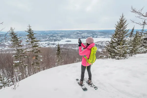 Telefon. Schneeschuhwanderin im Winterwald per Handy-App, die idyllische Winterlandschaft fotografiert. Menschen auf Wanderschaft im Schnee leben einen aktiven Lebensstil. Mont Tremblant, Laurentians, Quebec, Kanada — Stockfoto