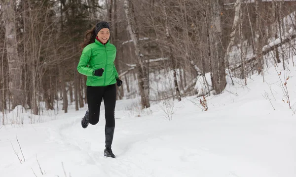 在冬雪中奔跑在森林里寒冷的冬日里,女跑步者在外面慢跑.将健康的生活方式理念与美丽的年轻健身模型相结合。亚洲白人长跑混合赛. — 图库照片