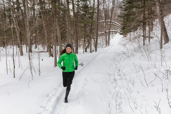 跑步的女运动员女赛跑选手穿着保暖的运动服和手套在寒冷的冬季森林里慢跑。美丽健康的亚洲白人女性健身模型 — 图库照片