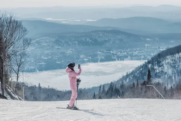 Vrouw maakt foto 's op skivakantie met de telefoon - Vrouw skiër met behulp van telefoon app op de skipiste nemen van foto' s van verbazingwekkende winter natuur landschap. Meisje met mobiele smartphone in geweldige ski-kleding — Stockfoto