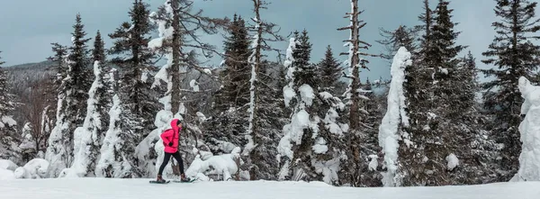 Snowshoeing mulher caminhando na neve na montanha da floresta. Atividade esportiva de inverno no frio ao ar livre snowshoe trilha caminhante andando sozinho na bandeira da paisagem — Fotografia de Stock