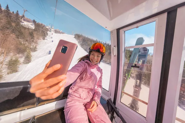 Urlop narciarski - kobieta narciarz w gondoli narciarskiej robi zdjęcie selfie lub wideo za pomocą telefonu. Koncepcja ferii zimowych. Narciarstwo na stokach śniegowych w górach. Ludzie dobrze się bawią w śnieżny dzień. Sporty zimowe — Zdjęcie stockowe