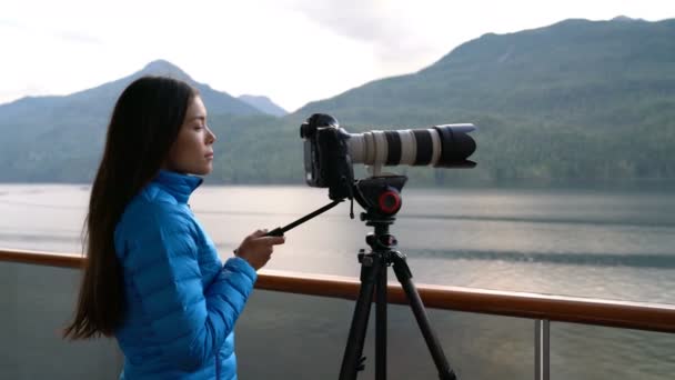 Travel photographer with professional telephoto lens camera on tripod shooting wildlife in Alaska, USA. Scenic cruising inside passage cruise tourist vacation adventure. Asian woman taking photo. — Video