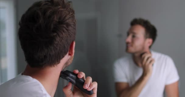 Man shaving beard using electric shaver trimmer. Male beauty grooming concept. — Stock video