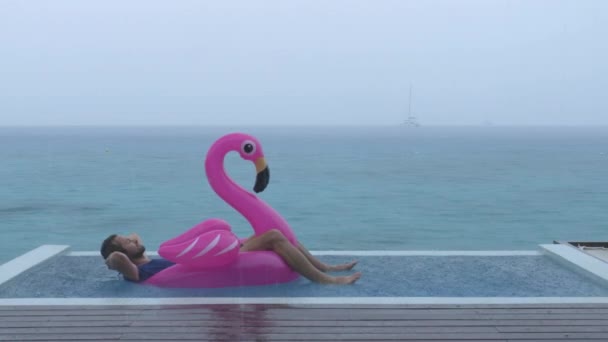 Vacation rain - funny video of man on flamingo float in luxury pool — стоковое видео