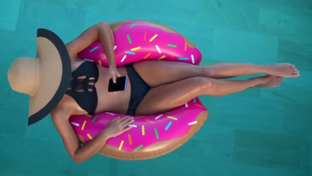 Mulher de férias de viagem em biquíni no donut inflável usando telefone na piscina — Vídeo de Stock