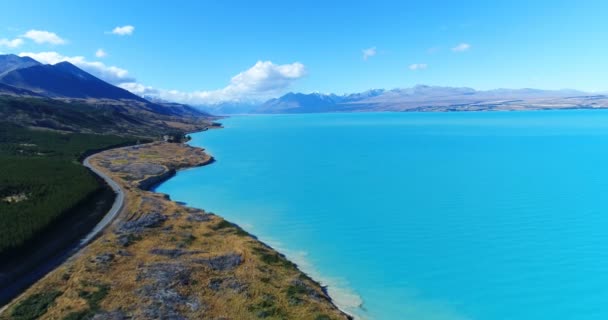 New Zealand aerial drone footage of lake Pukaki and southern alps on South Island. Road and clear blue lake with Aoraki Mount Cook National Park in background. New Zealand Tourist attraction — ストック動画
