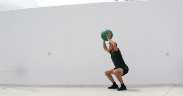 Fitness muž dělá dřepy s stropní medicíny míč tlačí na ramena. Tělesná cvičení cvičení fitness muž trénink nohy a hýždě s váženým medicína koule dřepy. Sportovec posiluje v posilovně — Stock video