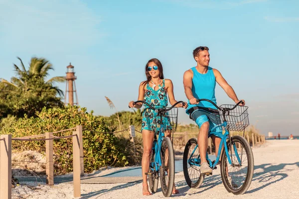 Biking activity couple tourists having fun doing outdoor sport on Florida beach vacation with rental bikes on Sanibel Island by the Lighthouse. woman with man friend riding bicycles outdoor lifestyle — стоковое фото