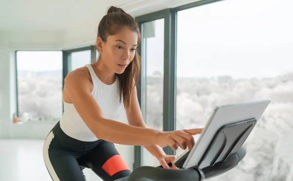 Home cycle workout Asian fit athlete woman training on stationary bike doing online cycling exercise class biking during livestream on screen — Fotografia de Stock