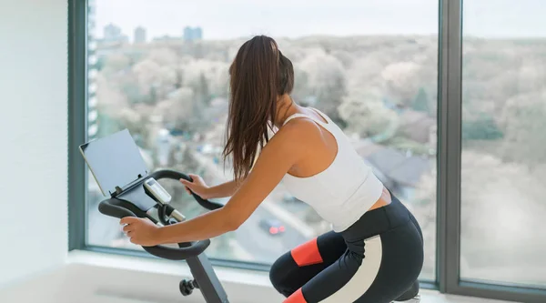 Spor salonunda spor yapan kadın, çevrimiçi beden eğitimi dersinde Cyle 'da kardiyo eğitimi alıyor. Sabit bisiklete binen kız. — Stok fotoğraf