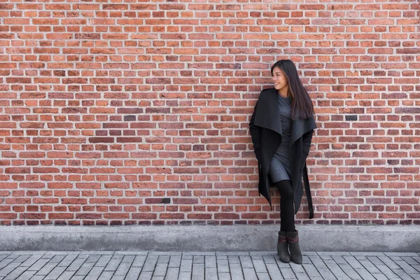 Asian young woman fashion model standing on street against brick wall background wearing winter wool coat and elegant dress for work — стокове фото