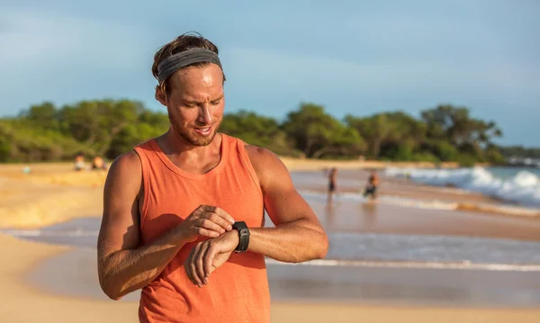 Corrida atleta homem usando aplicativo de fitness smartwatch no dispositivo de tecnologia wearable inteligente esportes assistir treinamento na praia. Corredor trabalhando suando no banner do dia de verão — Fotografia de Stock