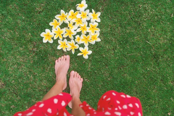 Pétalos de flores escapada romántica Hawaii viajes de vacaciones. Mujer POV caminando descalza sobre hierba de verano. Flores tropicales colocadas en el suelo para la boda al aire libre o belleza cuerpo cuidado de la piel pedicura —  Fotos de Stock