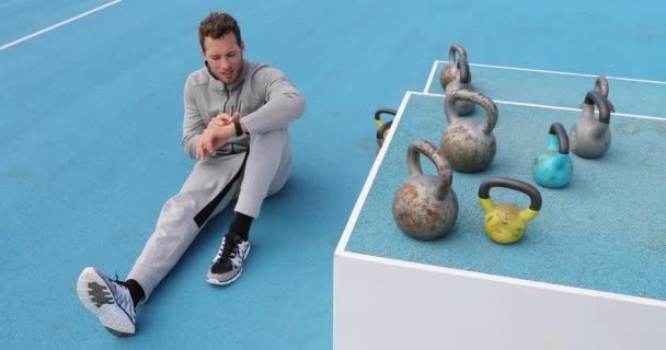 Fitnessman controleert smartwatch tijdens workout krachttraining op gewichtheffen kettlebells outdoor gym. Gezonde actieve levensstijl — Stockvideo