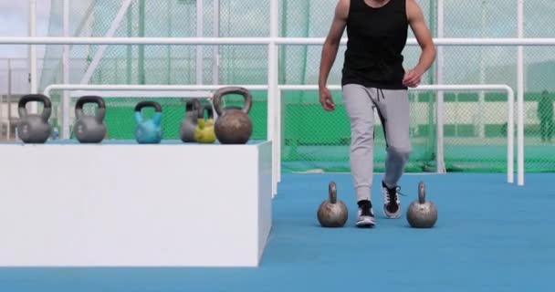 Fitness idrottsman gör bönder gå med kettlebells träning utomhus på Athletics stadion utomhus gym. Stark manlig idrottare styrketräning — Stockvideo