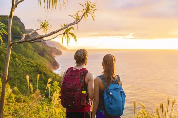 Hawaii hiking hikers hiking on Kalalau trail watching sunset from Na Pali Coast. Tourists couple with backpacks walking outdoor in Kauai island. Summer travel adventure active lifestyle