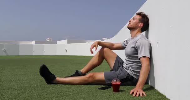 Yorgun bir sporcu sabahları antrenmandan sonra çimenlere oturup sağlıklı pancar suyu içiyor. — Stok video