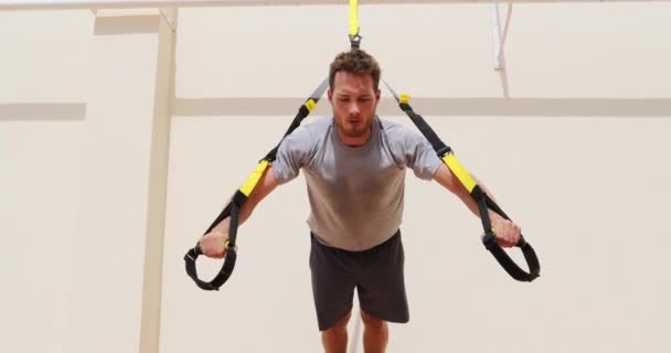 Hombre de fitness haciendo flexiones usando correas de suspensión en el gimnasio. Atleta haciendo ejercicios push-up de peso corporal al aire libre — Vídeos de Stock