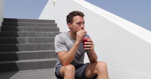 Saft-Smoothie-Sportler entspannen sich beim morgendlichen Frühstück nach dem Training auf dem Rasen zu Hause oder im Fitnessstudio. Sportler trinkt Smoothie mit roten Früchten — Stockvideo