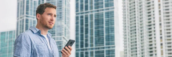 Telefoon levensstijl jongeman lopen naar het werk op pendelen zakenman met behulp van mobiele sms-bericht buiten in de stad straat met flatgebouwen skycrapers op de achtergrond — Stockfoto