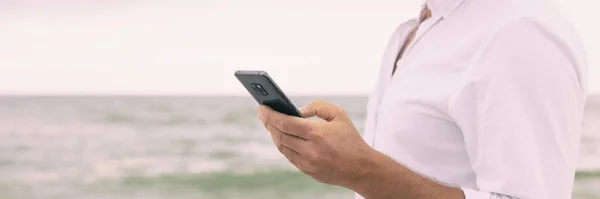 Telefone celular homem closeup de mão segurando smartphone mensagens de texto banner panorâmico. Empresário na praia usando dados de celular no panorama de férias de viagem — Fotografia de Stock