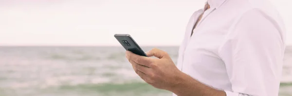 Mobile phone man closeup of hand holding smartphone texting panoramic banner. Businessman on beach using cellphone data on travel vacation panorama — Stock Photo, Image