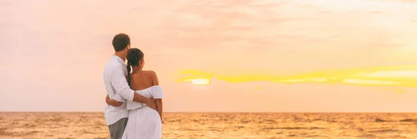 Smekmånad par promenader på romantisk kväll titta på solnedgång banner panorama bakgrund. Beach bröllop kvinna bär vit klänning och elegant man älskare koppla av på karibiska semester resor panoramautsikt — Stockfoto