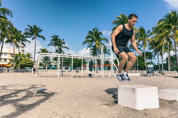 Kniebeuge springen auf der Trainingsbox in der Outdoor-Beach-Turnhalle. Mann Athlet beim Training auf Fitness Bank Springen außerhalb der Sommer amerikanischen South Beach Miami Stadt. Krafttraining für Männer, die draußen trainieren — Stockfoto