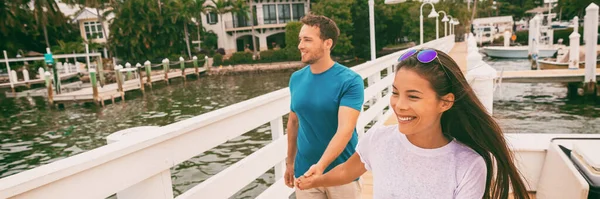Boldog fiatalok pár sétálnak a floridai sétányon Marina kikötői mólóján kéz a kézben. Fajok közötti kapcsolat Ázsiai lány, kaukázusi férfi élvezi a nyaralást. Panoráma felirat — Stock Fotó