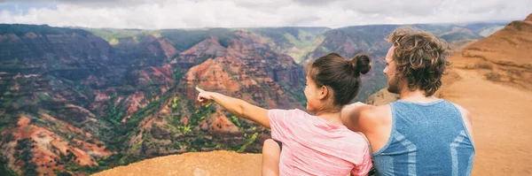 Gente haciendo senderismo en Hawái excursionistas de pancartas apuntando a las montañas Kauai. feliz excursionista pareja estilo de vida saludable al aire libre mirando Waimea vista del cañón. Parejas jóvenes en la naturaleza en Kauai, Hawaii, USA —  Fotos de Stock