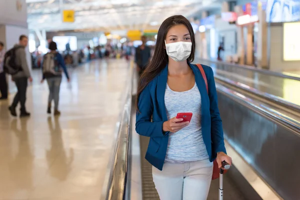 Reisepass Asiatische Touristin mit Maske am Flughafen mit Handy-App für den Impfnachweis während des Coronavirus-Pandemie-Urlaubs. Mädchen läuft im Terminal. — Stockfoto