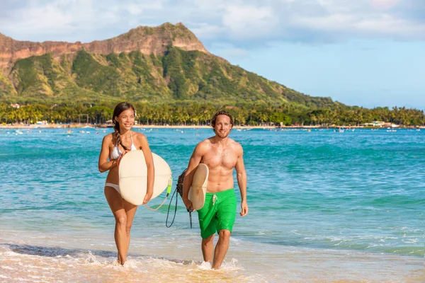 Surfistas havaianos casal surfar pessoas se divertindo surfando na praia de Waikiki, Honolulu, ilha de Oahu, Havaí. Mulher asiática, homem caucasiano interracial grupo de amigos correndo para fora do oceano carregando pranchas de surf — Fotografia de Stock