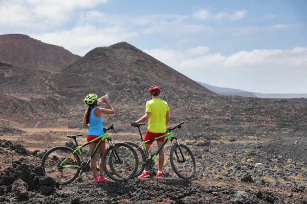 Biking adventure mountain MTB bikes cyclist cycling on extreme lava volcanic landscape. Two bikers in guided group tour on summer vacation in Lanzarote, Canary Islands, Spain. — Stock Photo, Image