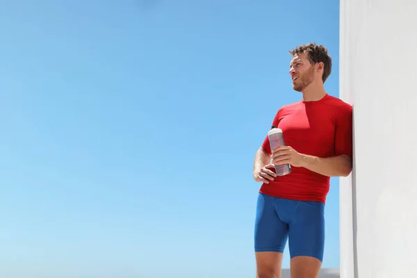 Gezonde fitnessman vermoeid drinkwaterfles uitgedroogd na training thuis — Stockfoto